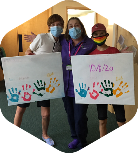 Picture of Ethan and Jared with Amanda, a nurse on the unit. Both boys are holding handprint memory canvases.
